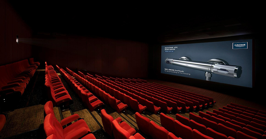 Audience seated in a darkened multiplex hall viewing pre-show cinema advertising on a large screen